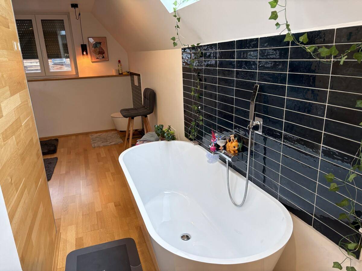 Elegantes Badezimmer mit freistehender Badewanne, dunklen Fliesen und Dachfenster.