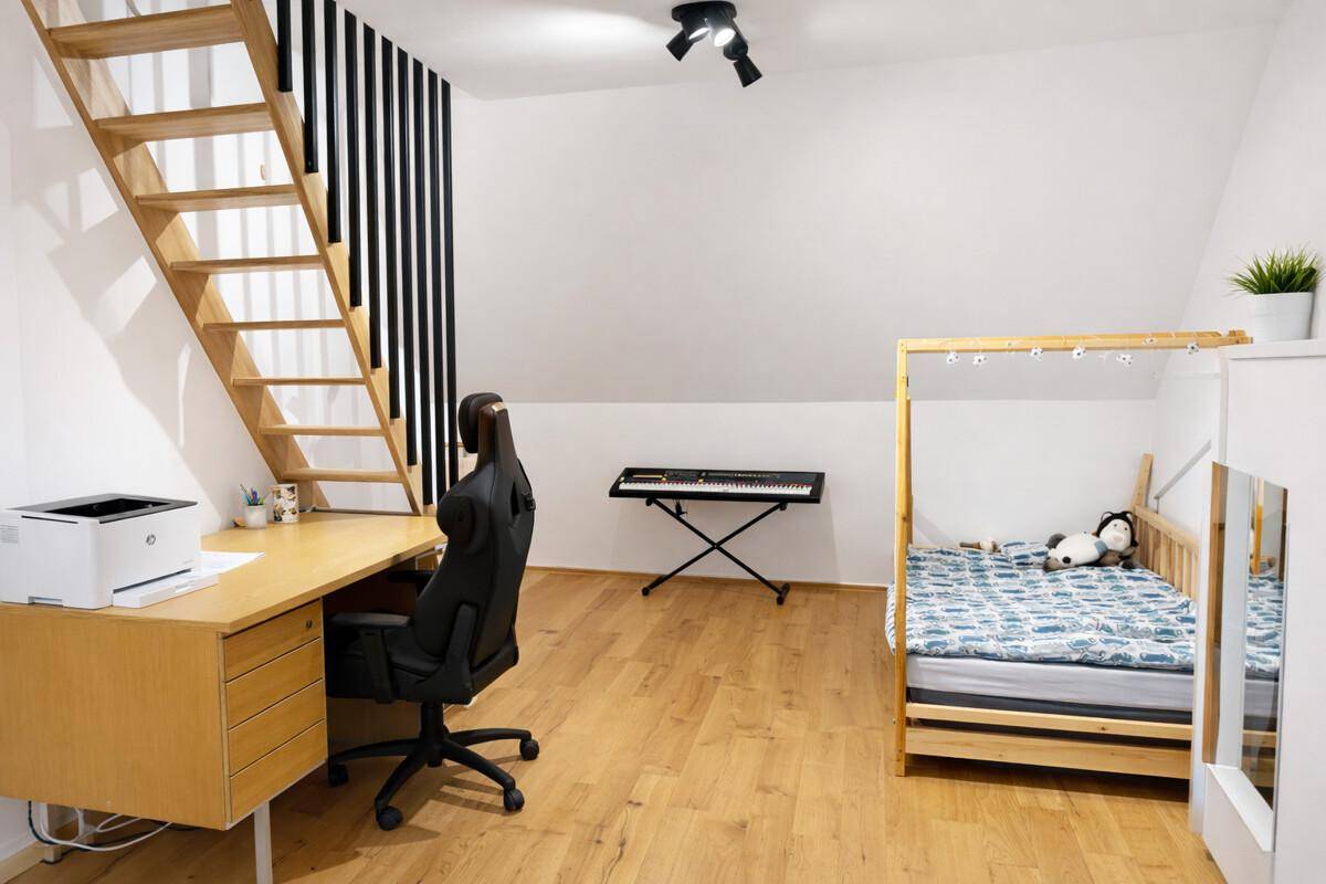 Helles Zimmer im Dachgeschoss mit Holzboden, Schreibtisch und Zugang zu einer weiteren Ebene.