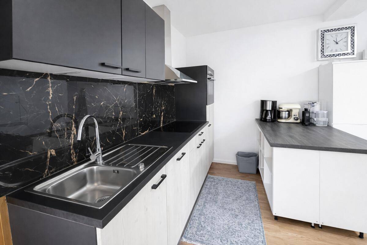 Moderne Küche mit schwarzen Schränken, Marmor-Rückwand und Edelstahlspüle.