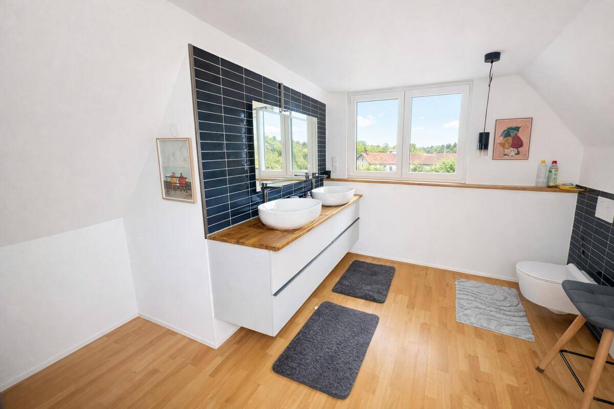 Modernes Badezimmer im Dachgeschoss mit Doppelwaschbecken, dunklen Fliesen und Fenster.