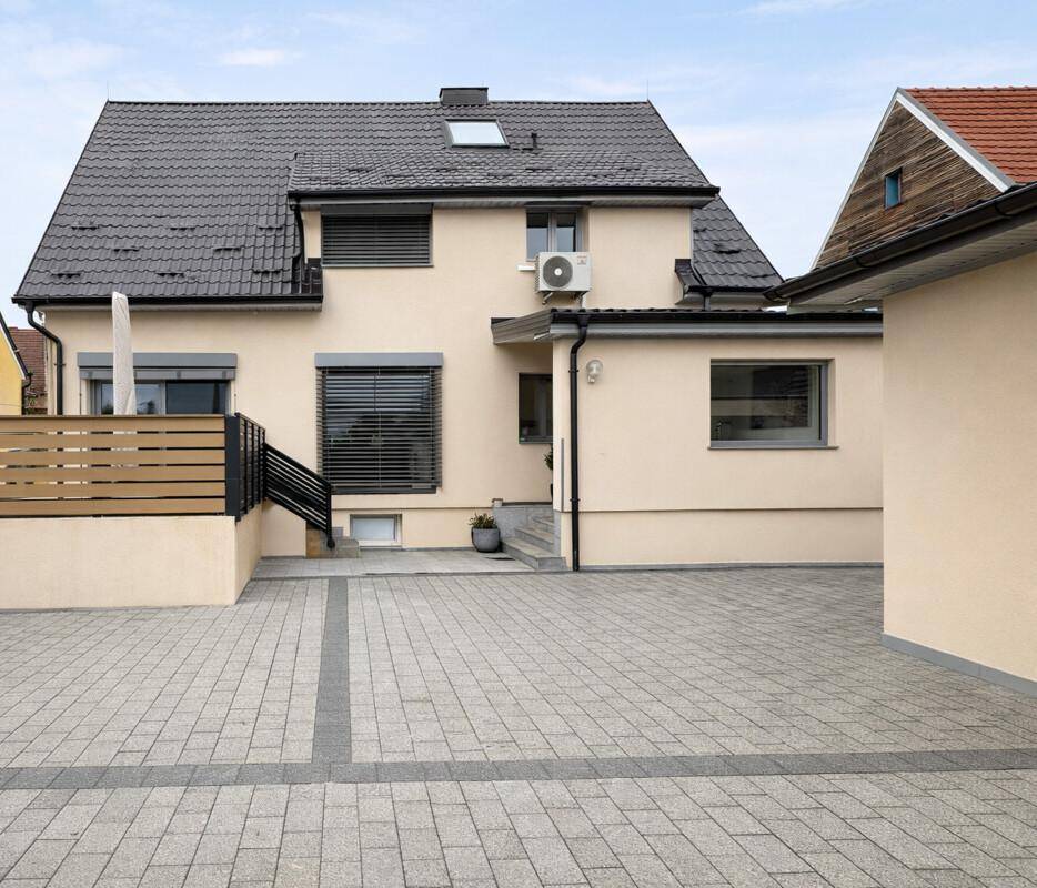 Rückansicht des modernen Hauses mit gepflastertem Hof und Klimaanlage an der Fassade.