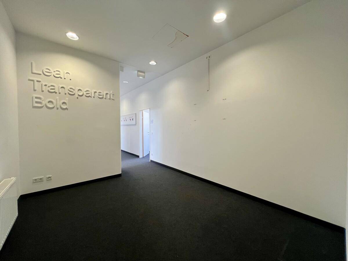 Heller Flur mit weißer Wand und einem inspirierenden Schriftzug, der zu weiteren Büroräumen führt.