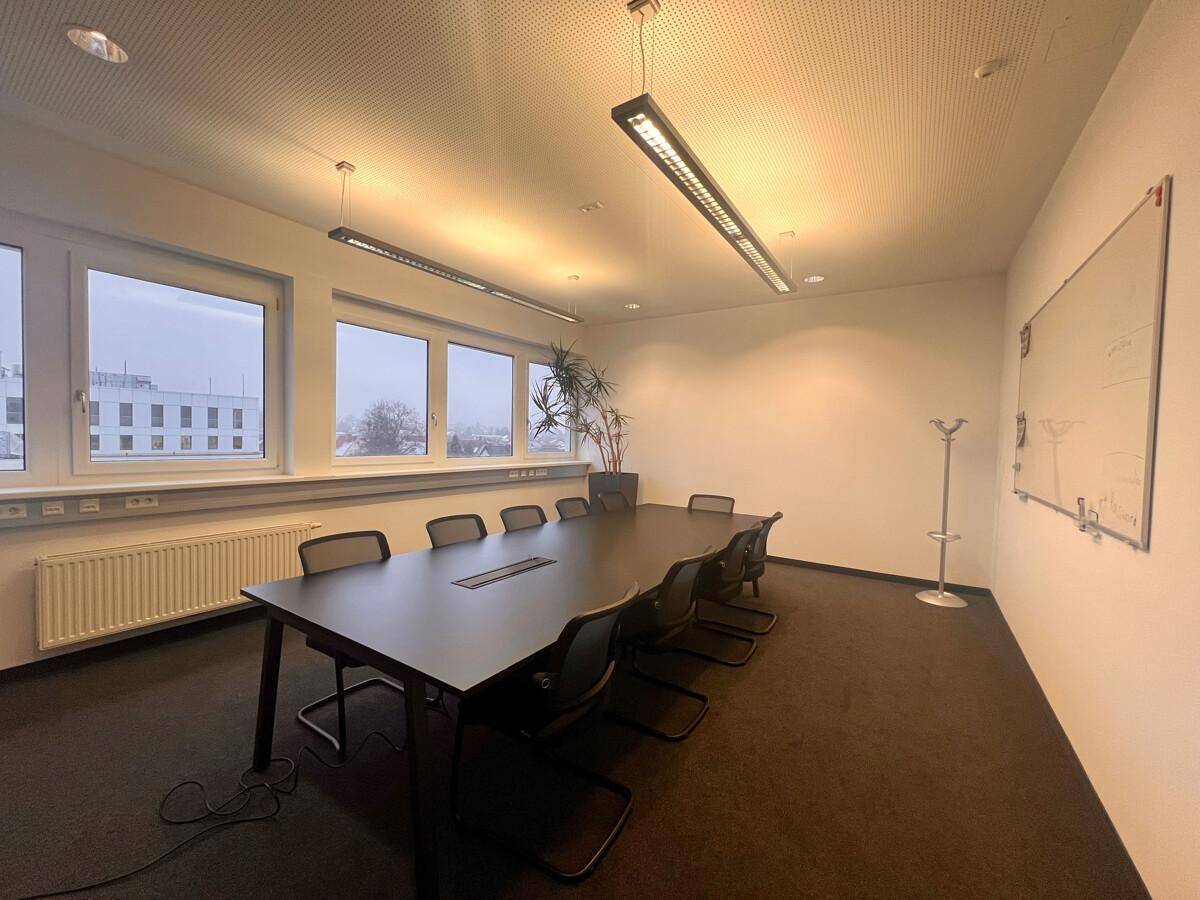 Geräumiger Konferenzraum mit großem Tisch, Stühlen und Fenstern, die einen Blick nach draußen ermöglichen.