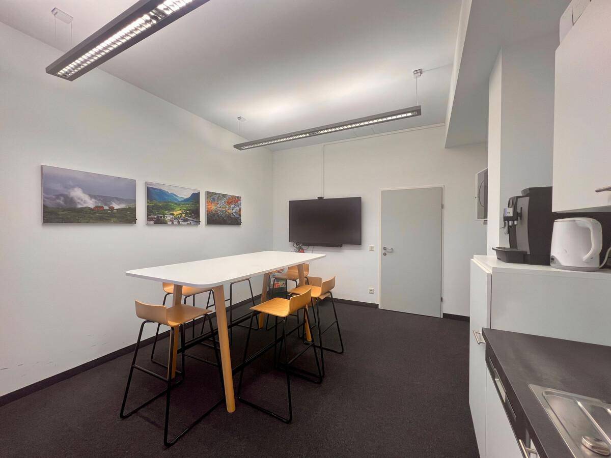 Heller Pausenraum mit einer Küchenzeile, einem Stehtisch und Barhockern, ideal für informelle Treffen.