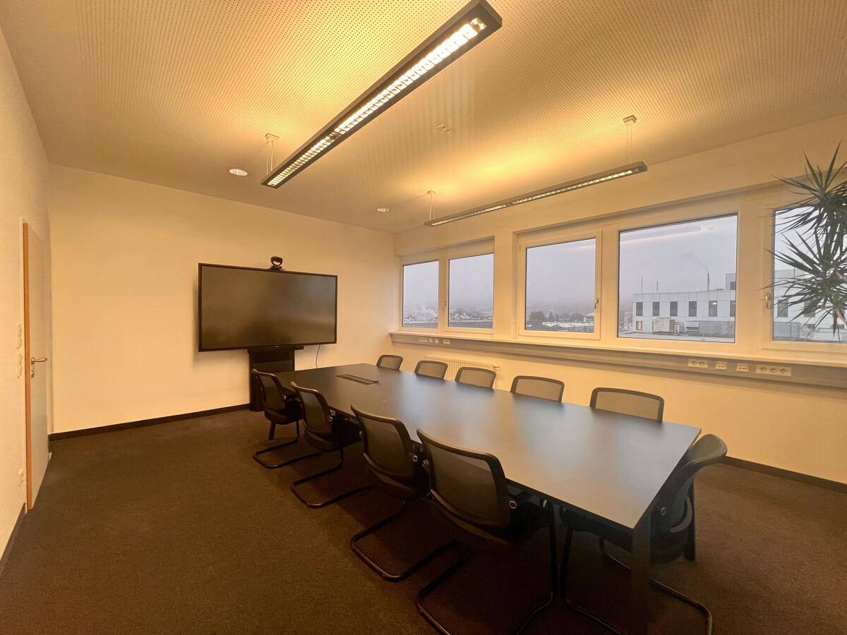 Moderner Konferenzraum mit großem Tisch, Stühlen und einem Wandfernseher, ideal für geschäftliche Treffen.
