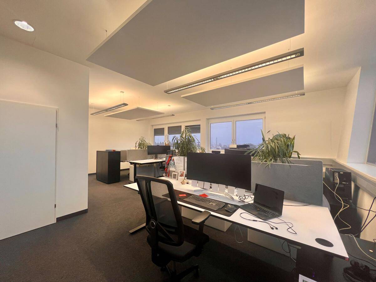 Geräumiger Büroraum mit mehreren Arbeitsplätzen, Schreibtischen und ergonomischen Stühlen, ideal für Teamarbeit.