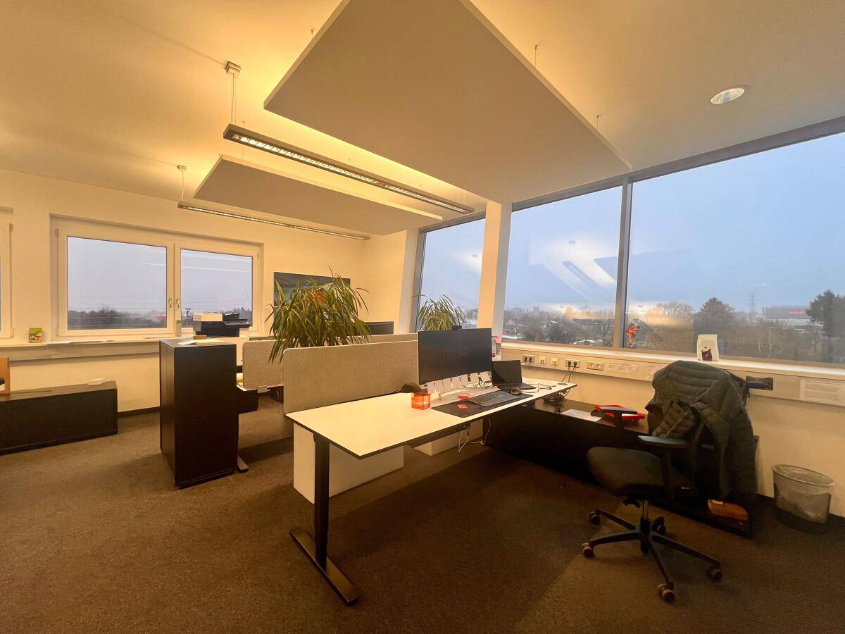 Offener Büroraum mit mehreren Arbeitsplätzen, Schreibtischen und ergonomischen Stühlen, mit Blick nach draußen.