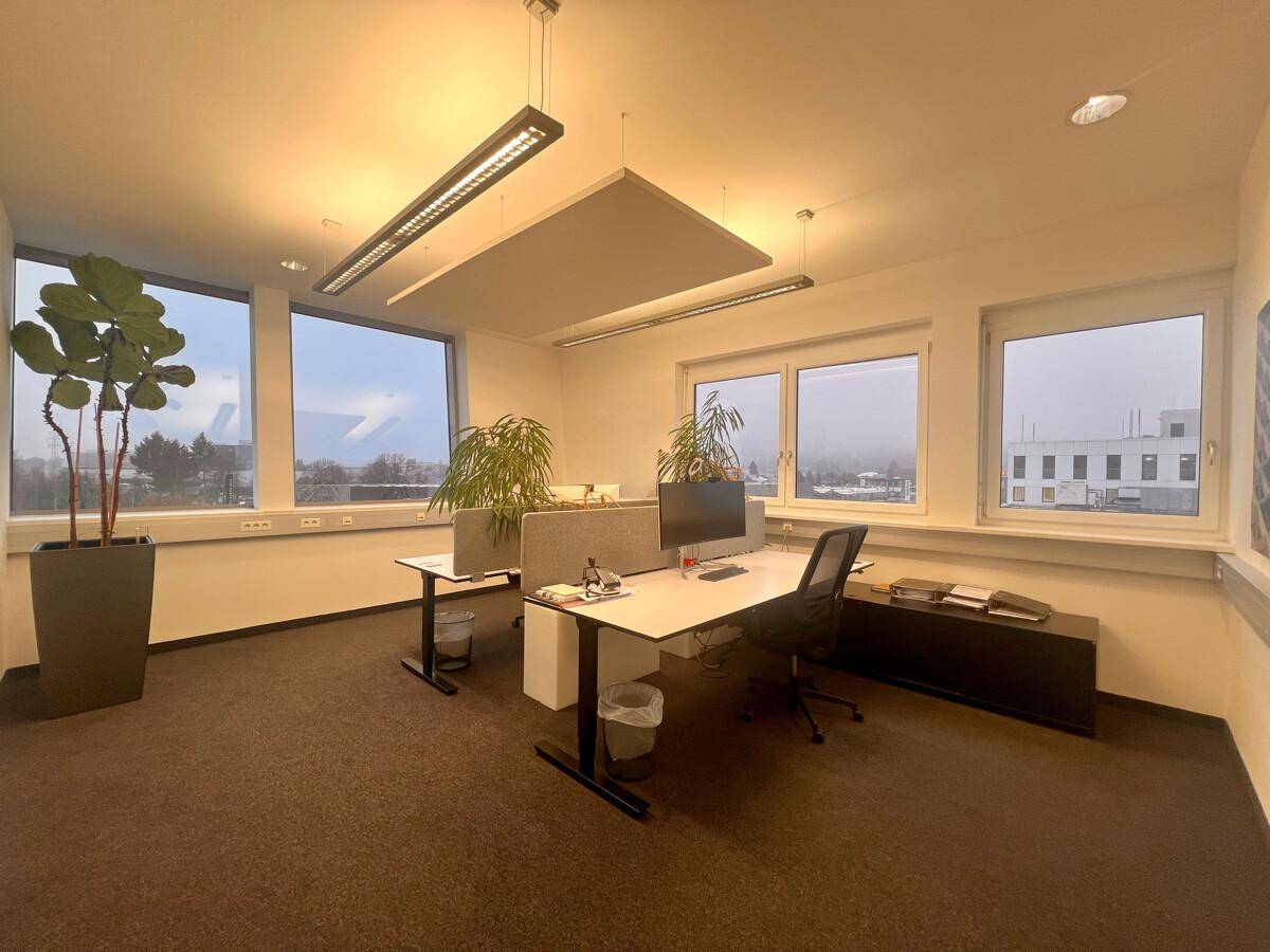 Geräumiger Büroraum mit mehreren Arbeitsplätzen, Schreibtischen und ergonomischen Stühlen, mit Blick nach draußen.