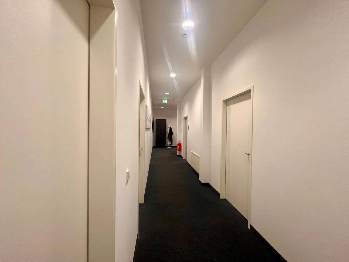 Heller Flur mit mehreren Türen, die zu verschiedenen Büroräumen führen, und dunklem Teppichboden.