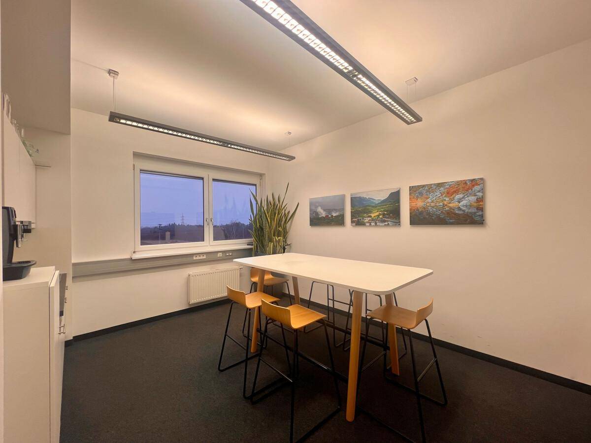 Gemütlicher Pausenraum mit einer Küchenzeile, einem Stehtisch und Barhockern, ideal für informelle Treffen.