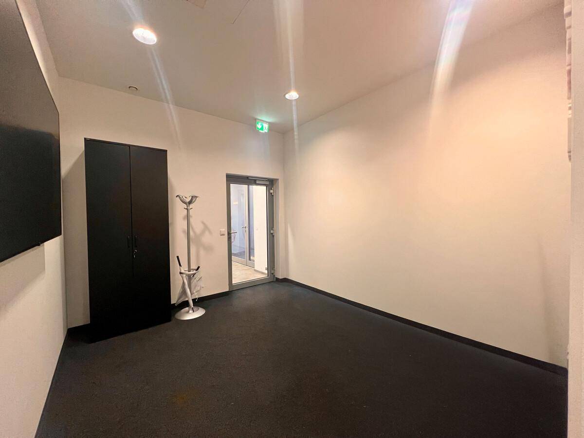 Heller Eingangsbereich mit dunklem Teppichboden und einer Glastür, die den Zugang zum Gebäude ermöglicht.