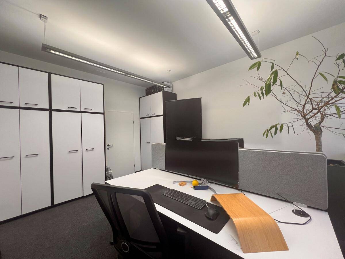 Moderner Büroraum mit Arbeitsplatz, Schreibtisch und ergonomischem Stuhl, umgeben von weißen Schränken für Stauraum.