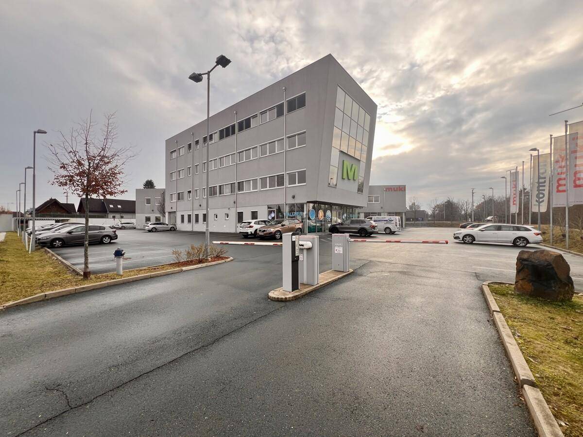 Modernes Bürogebäude mit markanter Architektur und großem Außenparkplatz, umgeben von Bäumen.