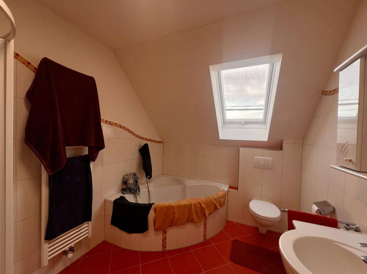 Badezimmer mit Eckbadewanne, Dachfenster und Fliesenboden in hellem Design.