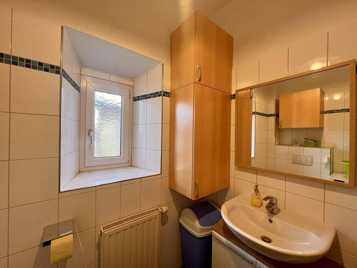 Gäste-WC mit Waschbecken, Spiegel und Fenster für natürliche Belüftung.