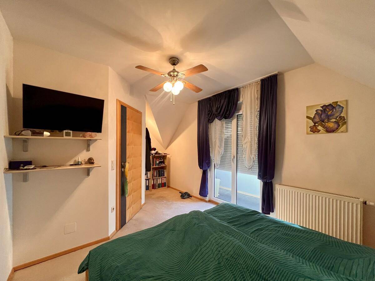 Schlafzimmer mit Dachschräge, Deckenventilator und Zugang zum Balkon.