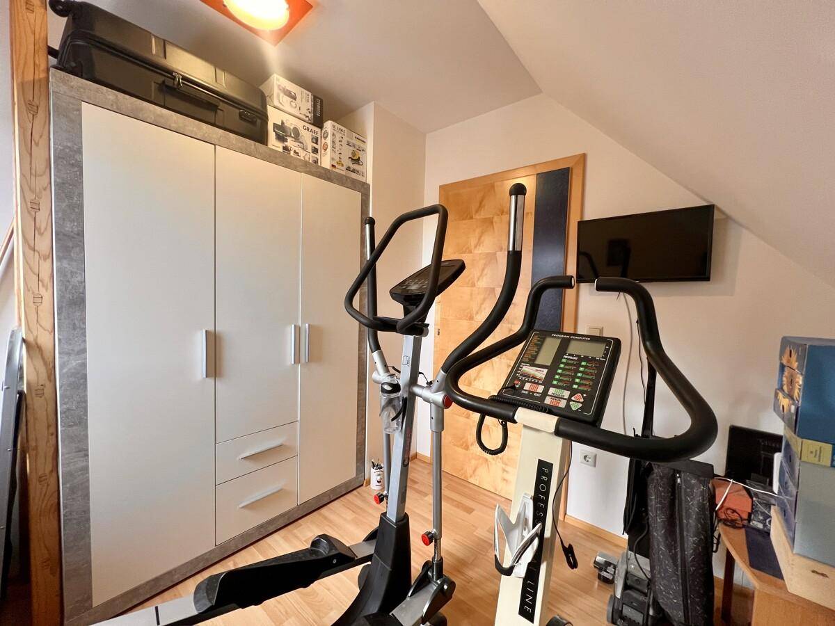Fitnessraum mit Trainingsgeräten, Schrank und Holzboden für sportliche Aktivitäten.