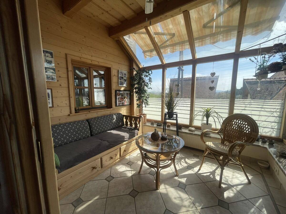 Heller Wintergarten mit Holzwänden, Fliesenboden und Blick ins Grüne.