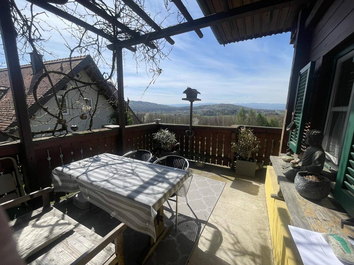 Überdachte Terrasse mit Holztisch, Stühlen und weitem Blick über die Landschaft.