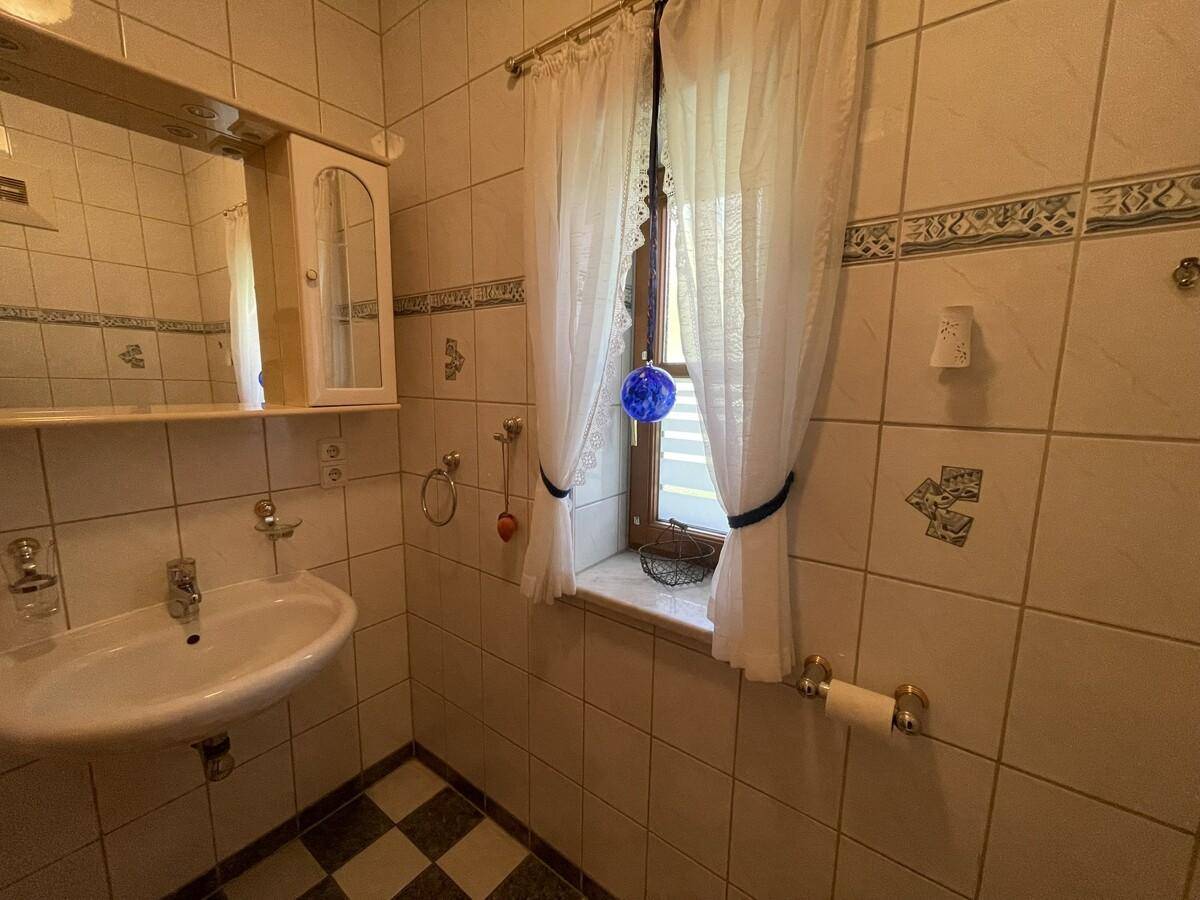 Kleines Gäste-WC mit Fenster, Waschbecken und kariertem Fliesenboden.