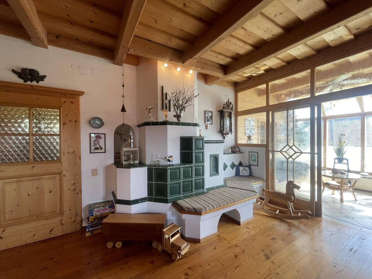Gemütlicher Wohnbereich mit Kachelofen, Holzboden und Zugang zum Wintergarten.