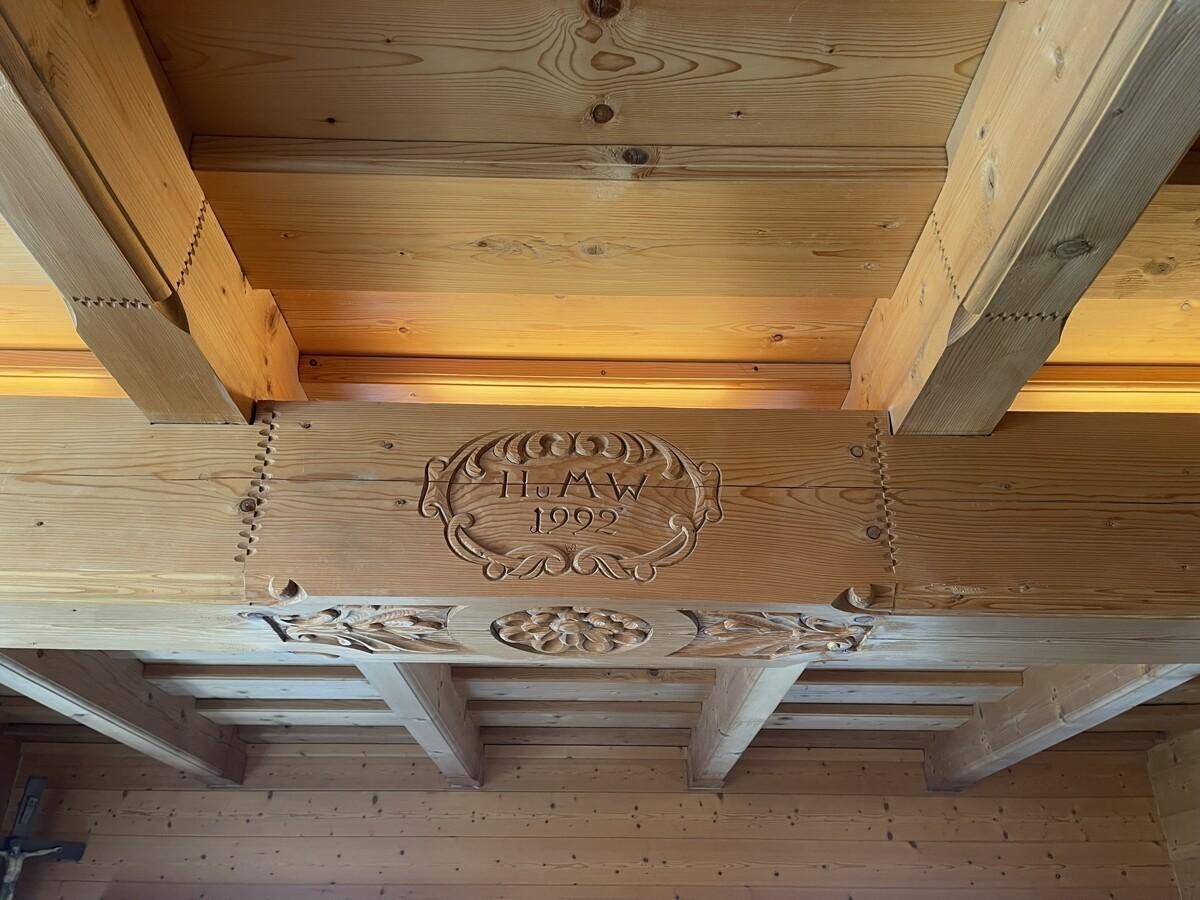 Detailaufnahme einer kunstvoll geschnitzten Holzbalkendecke mit Jahreszahl 1992.