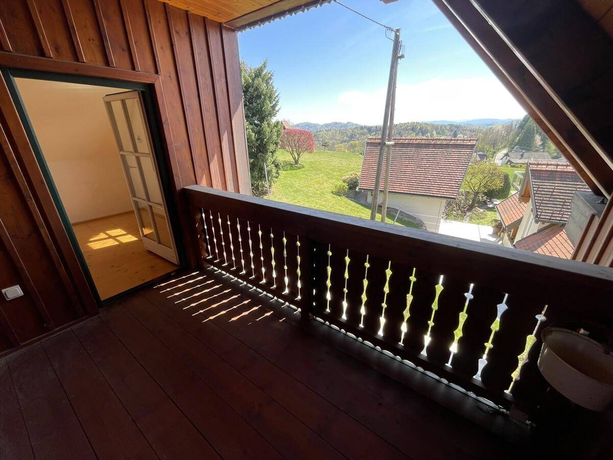 Kleiner Holzbalkon mit Blick auf die grüne Landschaft und benachbarte Häuser.