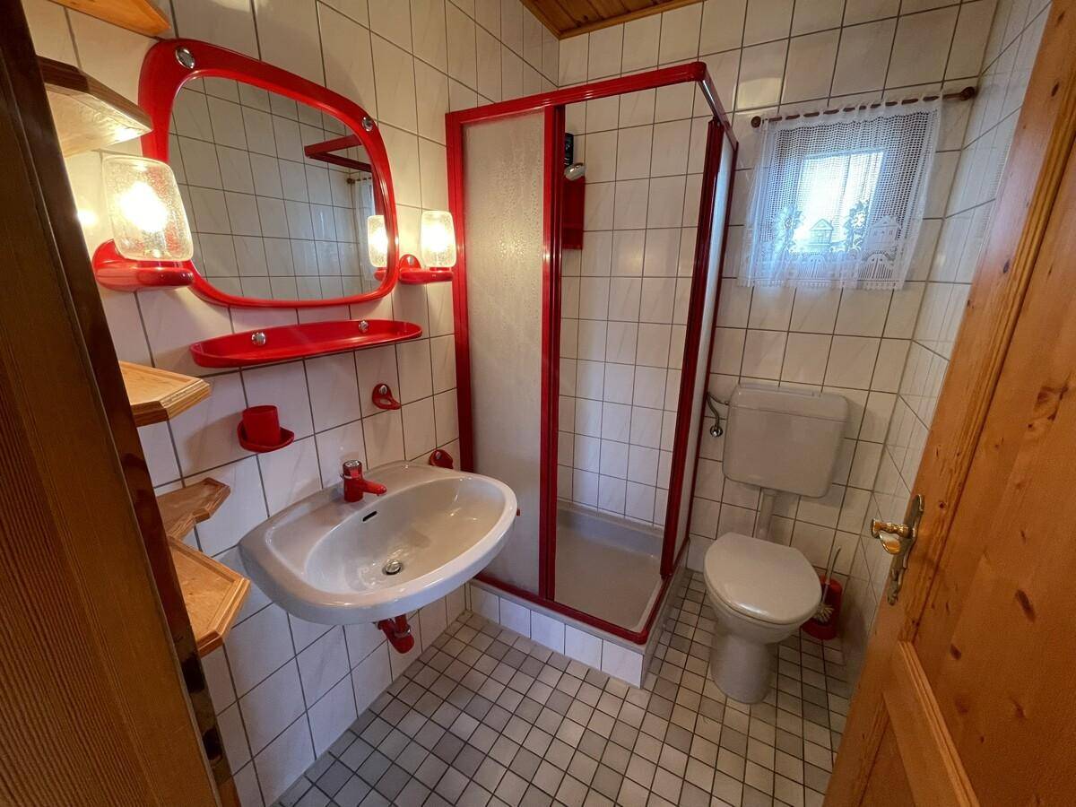 Kleines Badezimmer mit Duschkabine, Waschbecken und roten Akzenten.
