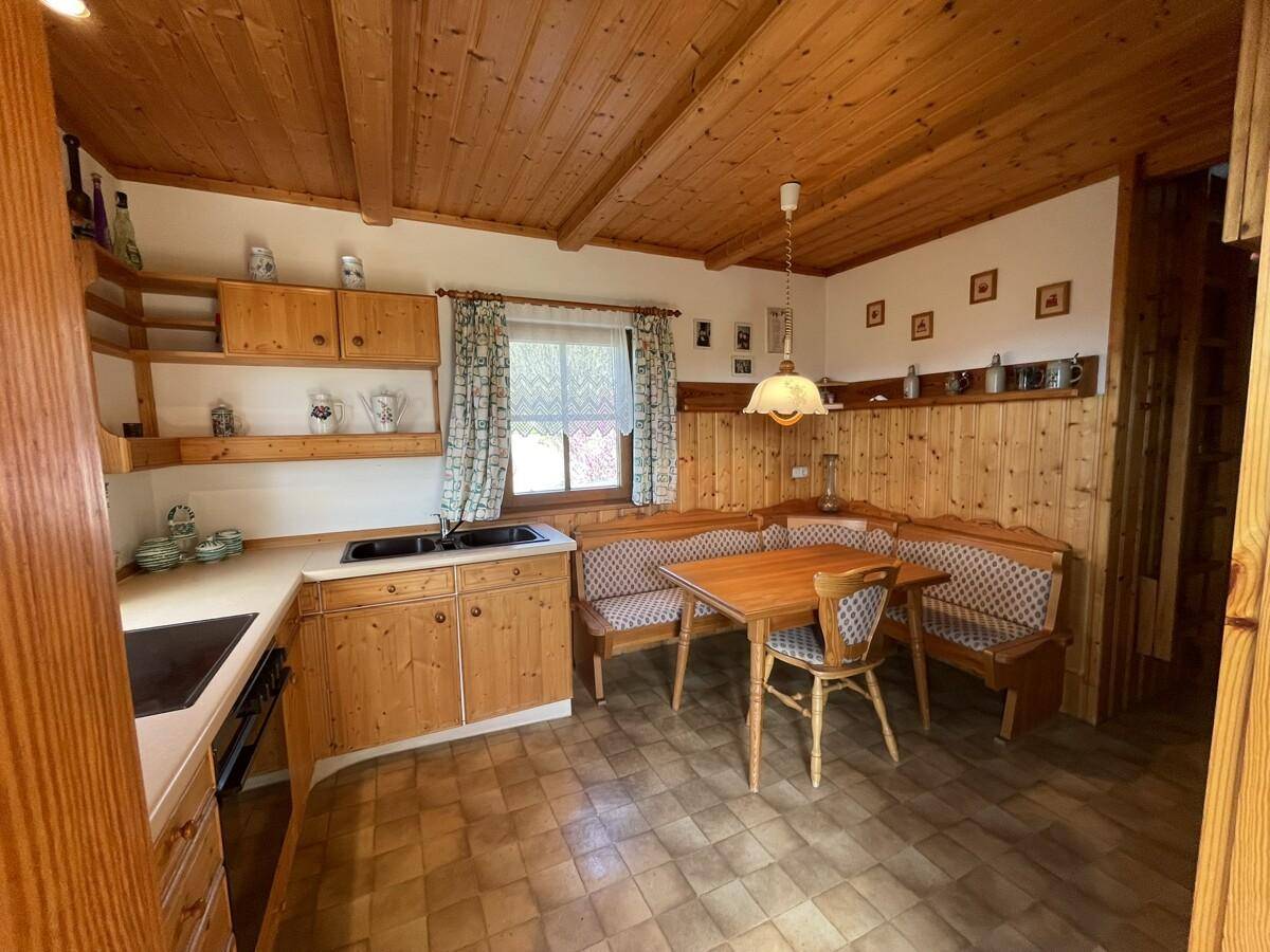 Rustikale Küche mit Holzschränken, Essbereich und Holzbalkendecke.