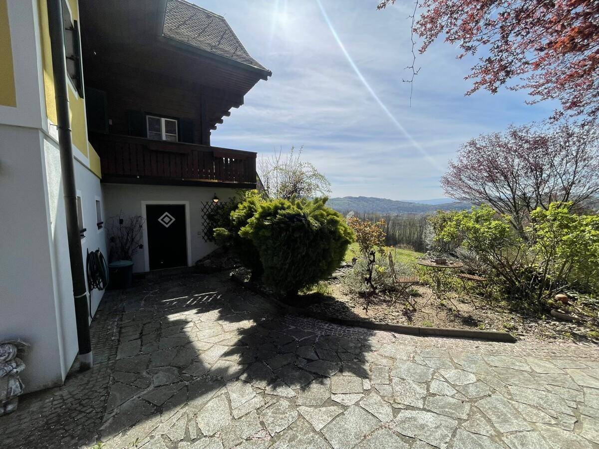 Gepflasterter Weg zum Haus mit Gartenbereich und Blick auf die Landschaft.