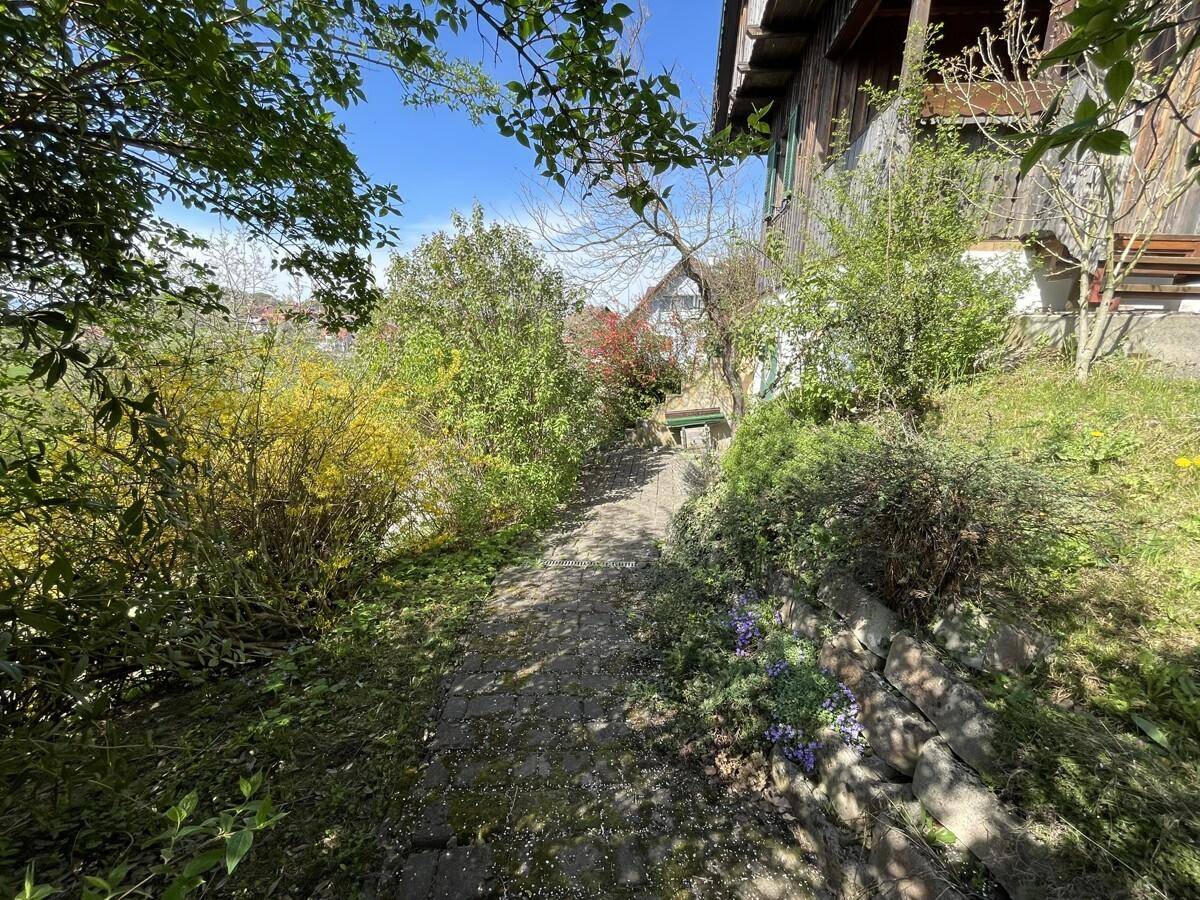 Schmaler Gartenweg zwischen üppiger Vegetation und einer Steinmauer.