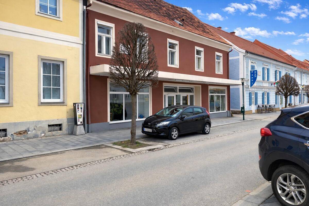 Ansicht des Gebäudes mit roter Fassade und angrenzenden Häusern entlang einer ruhigen Straße.