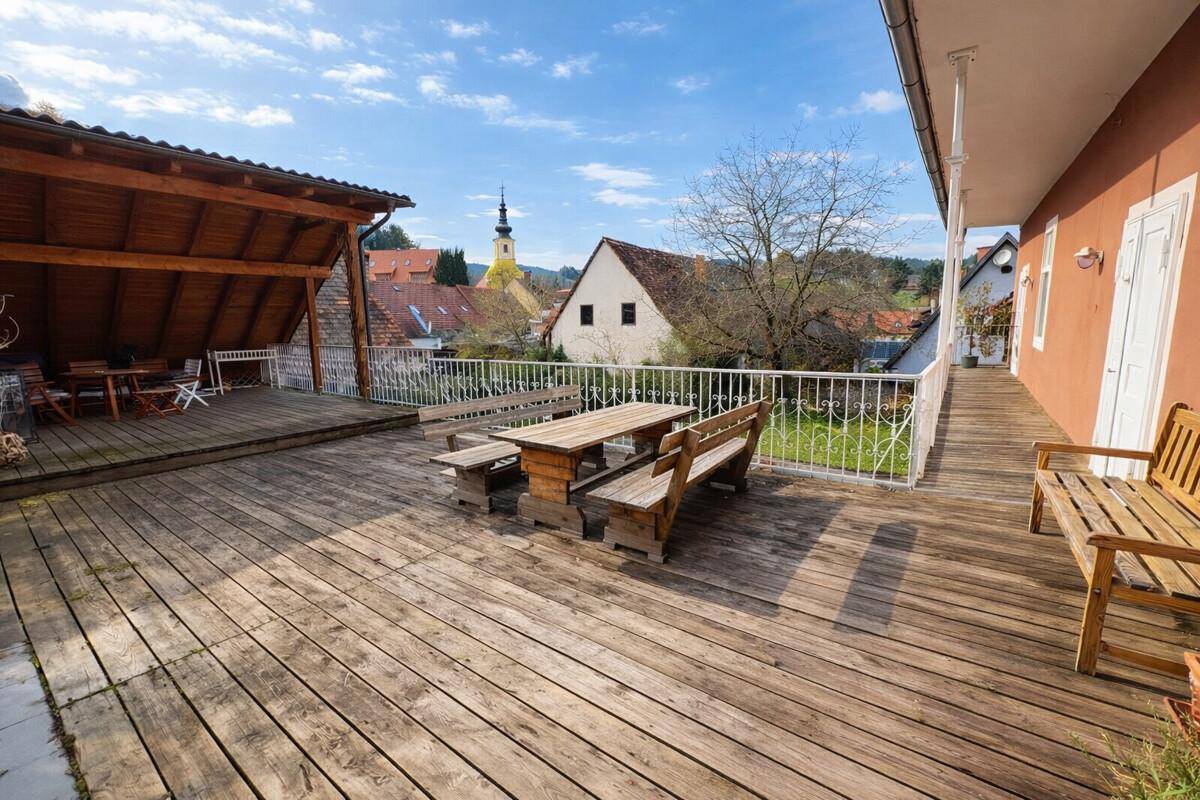 Große Holzterrasse mit rustikalen Gartenmöbeln und weitem Blick über die Dächer der Umgebung.
