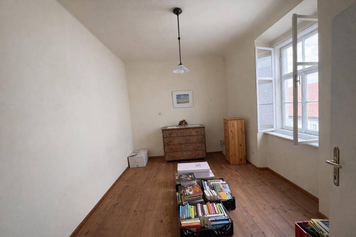Helles Schlafzimmer mit Holzdielenboden, Kommode und Blick nach draußen.