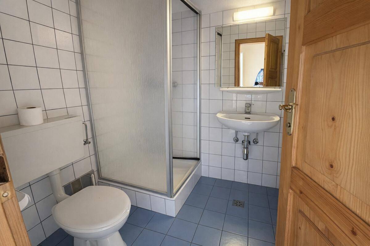 Kleines Badezimmer mit Dusche, WC, Waschbecken und blauen Fliesen.