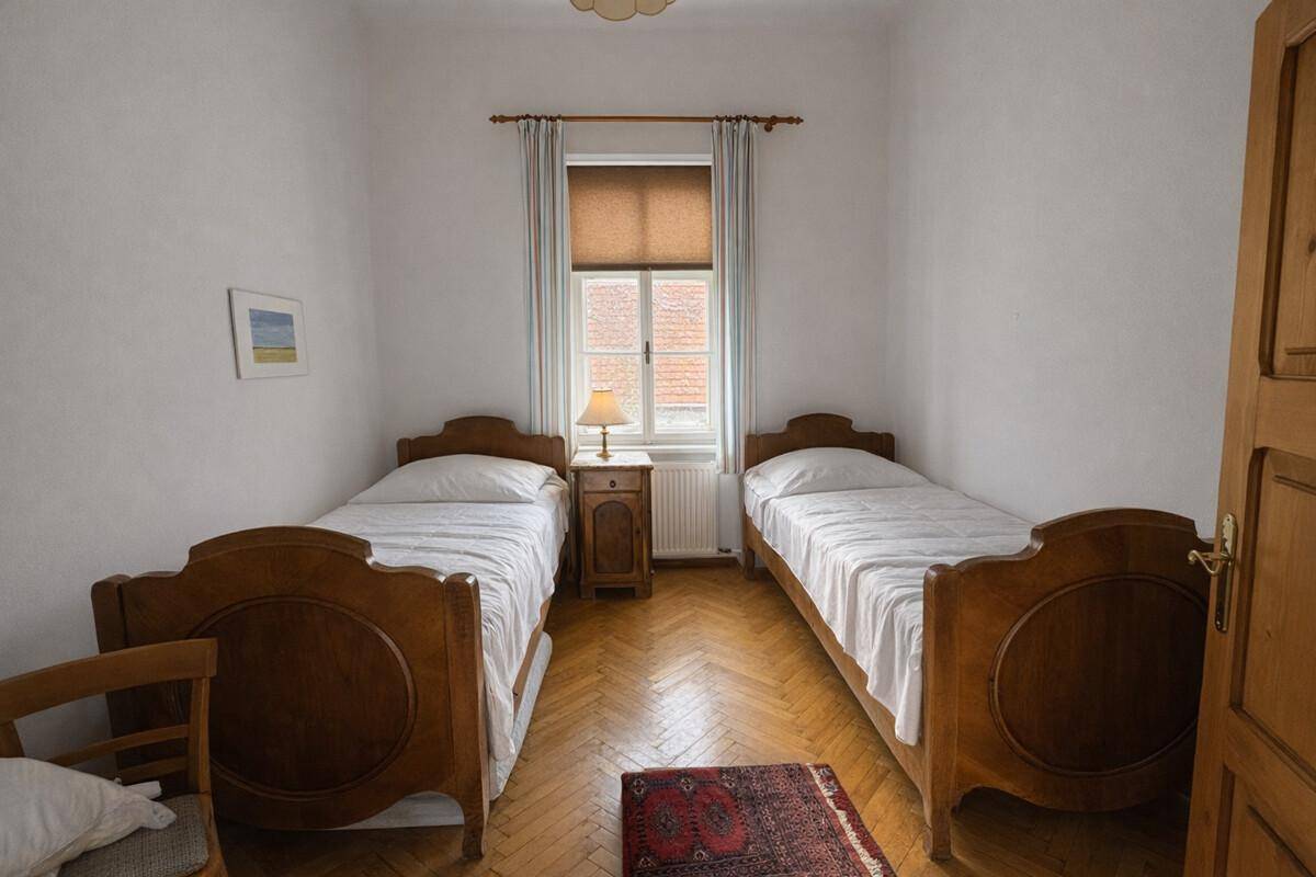 Schlafzimmer mit zwei Einzelbetten, Fischgrätparkett und Fenster mit Rollo.