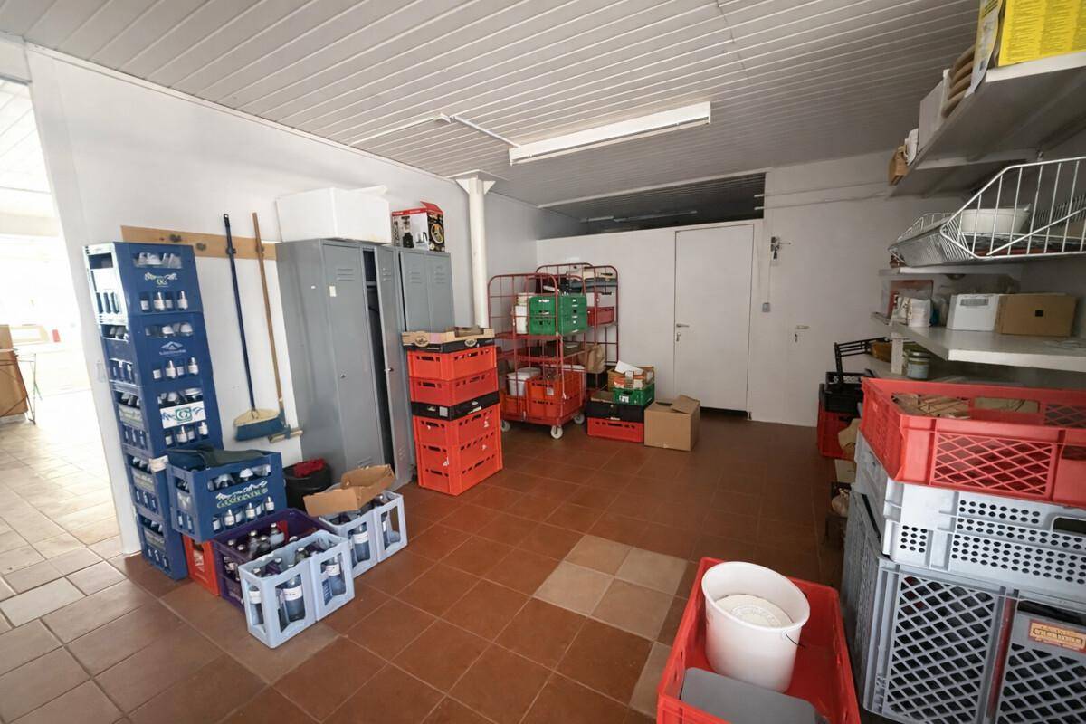 Lagerraum mit Regalen, Kisten und Fliesenboden für diverse Vorräte.