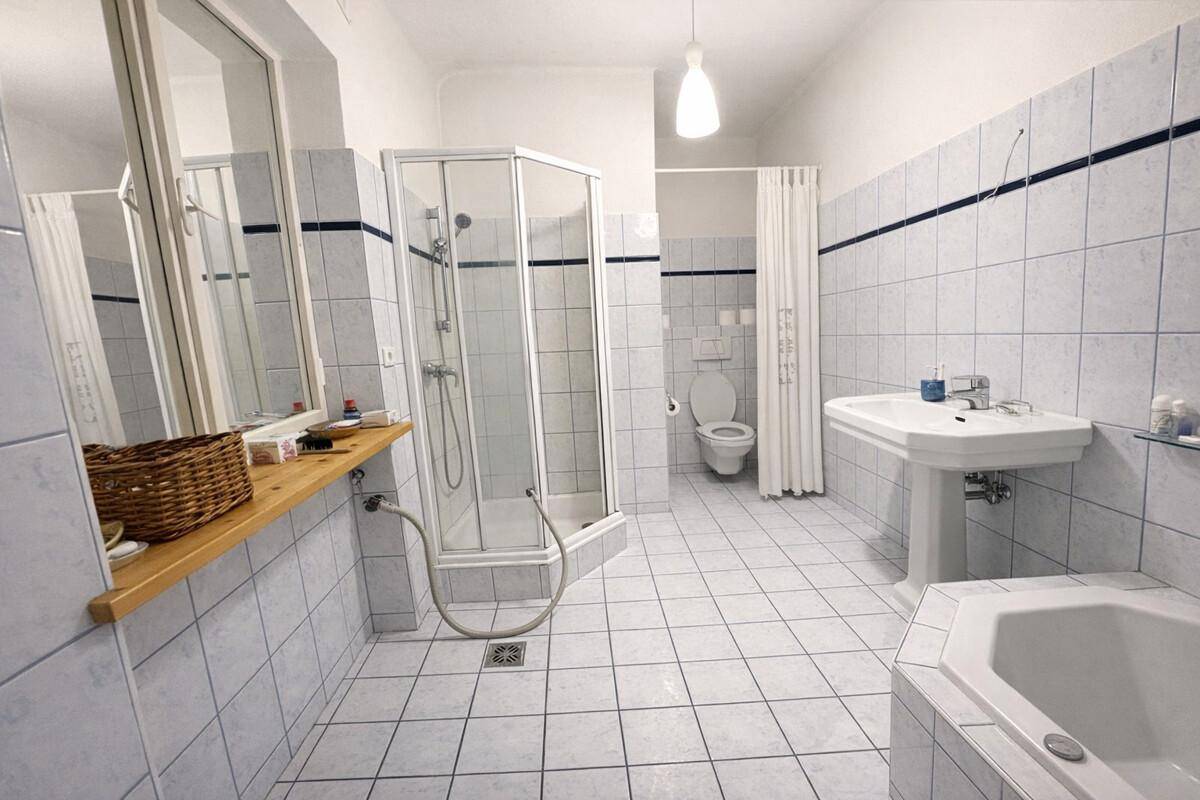 Geräumiges Badezimmer mit Dusche, Badewanne, WC und hellblauen Fliesen.