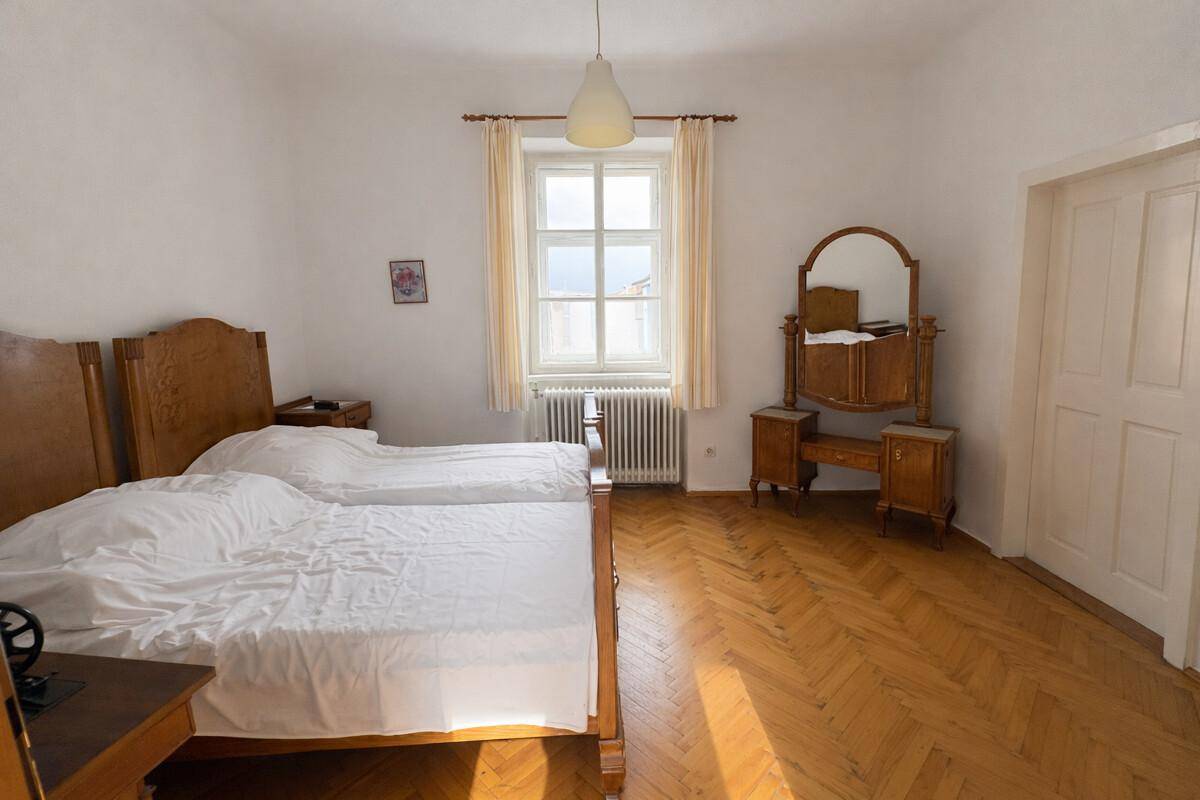Helles Schlafzimmer mit Doppelbett, Holzparkett und antiker Kommode.