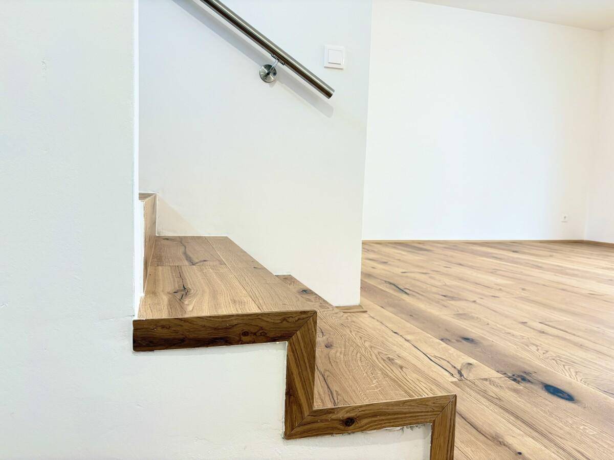 Detailansicht der modernen Holztreppe mit Edelstahlgeländer, die den Übergang zum Wohnbereich bildet.