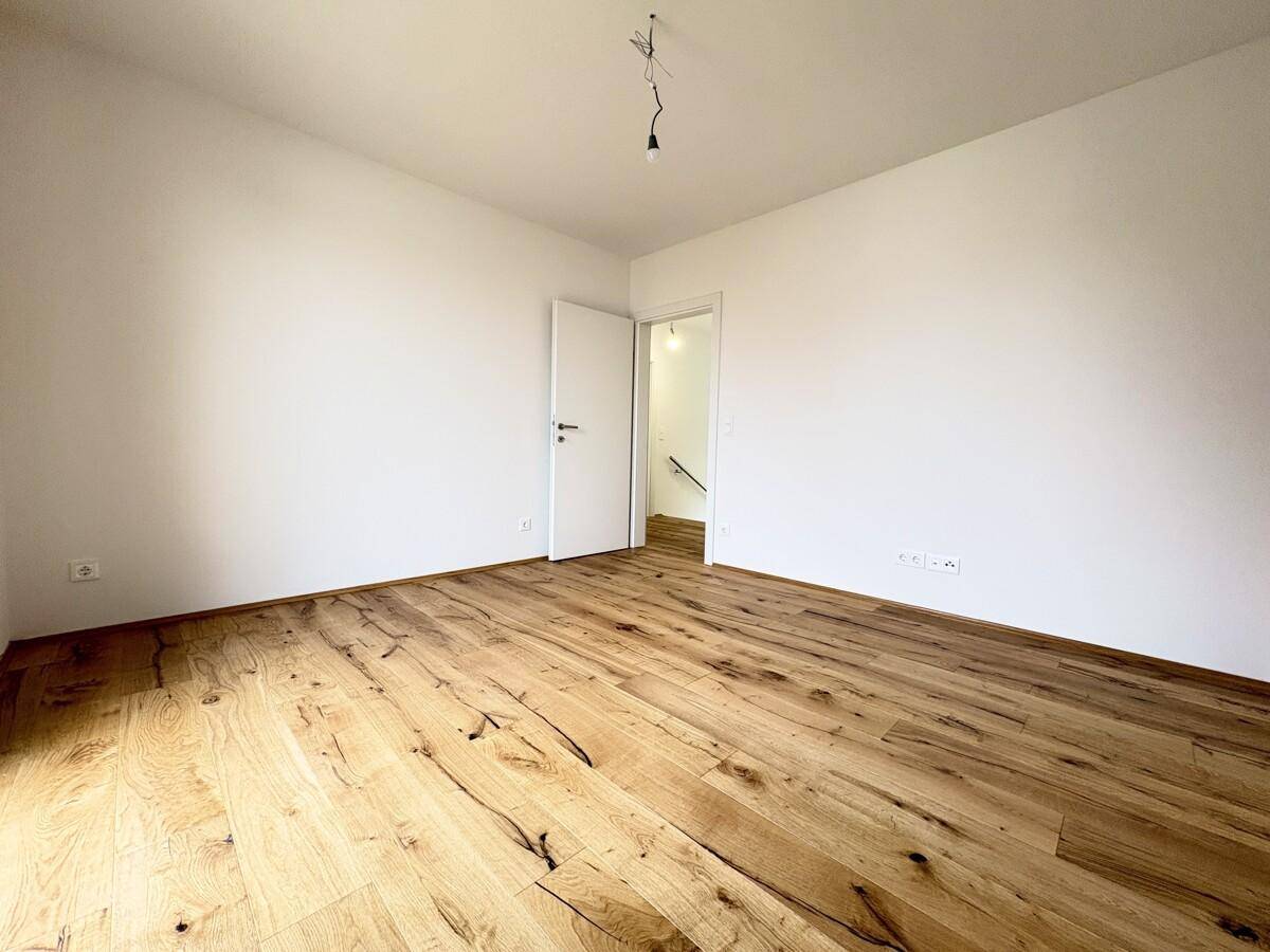 Helles, leeres Zimmer mit neuem Holzboden und weiß gestrichenen Wänden, bereit zur individuellen Gestaltung.