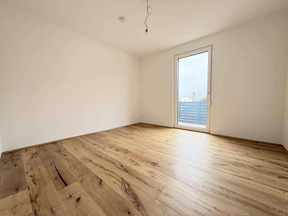 Geräumiges Schlafzimmer mit Holzboden und Zugang zu einem Balkon, der viel Tageslicht hereinlässt.