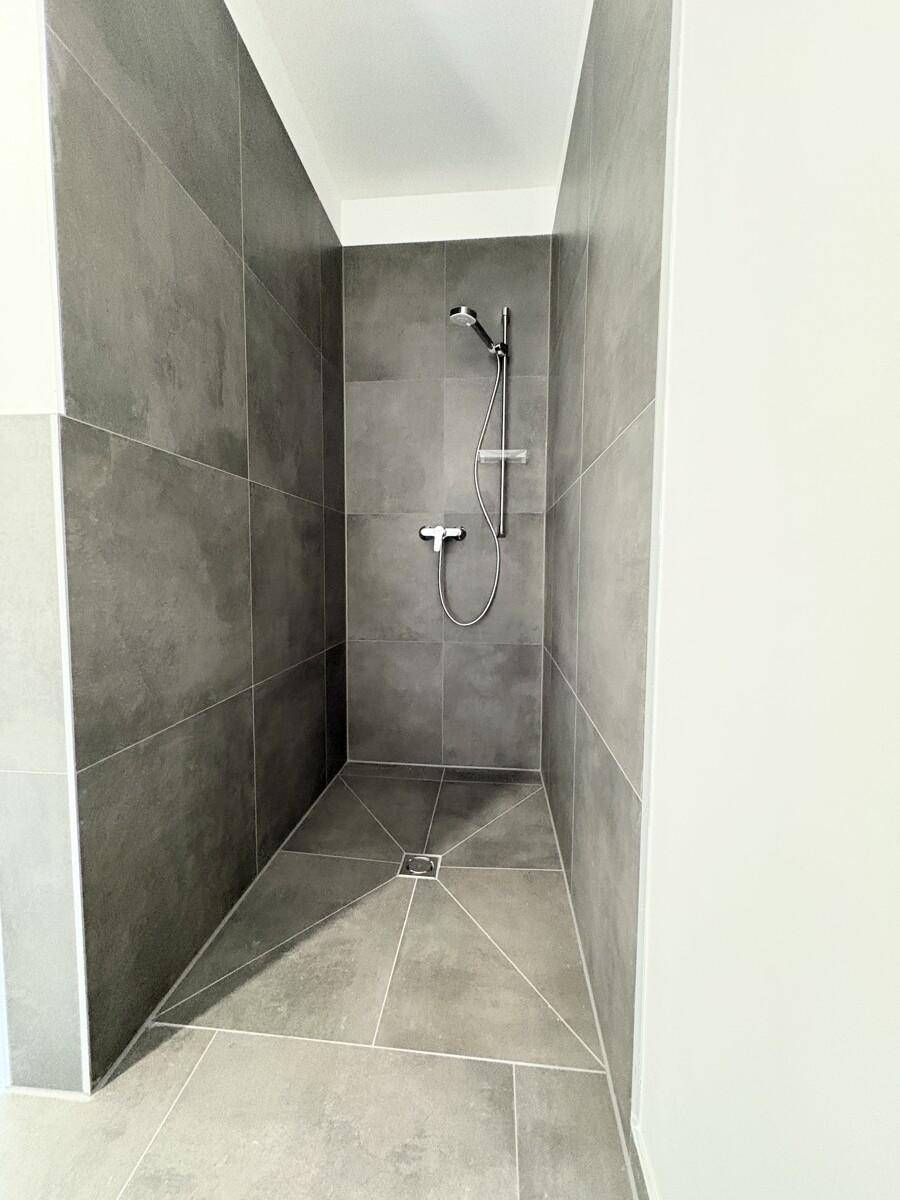 Modernes Badezimmer mit großformatigen grauen Fliesen und einer ebenerdigen Dusche.