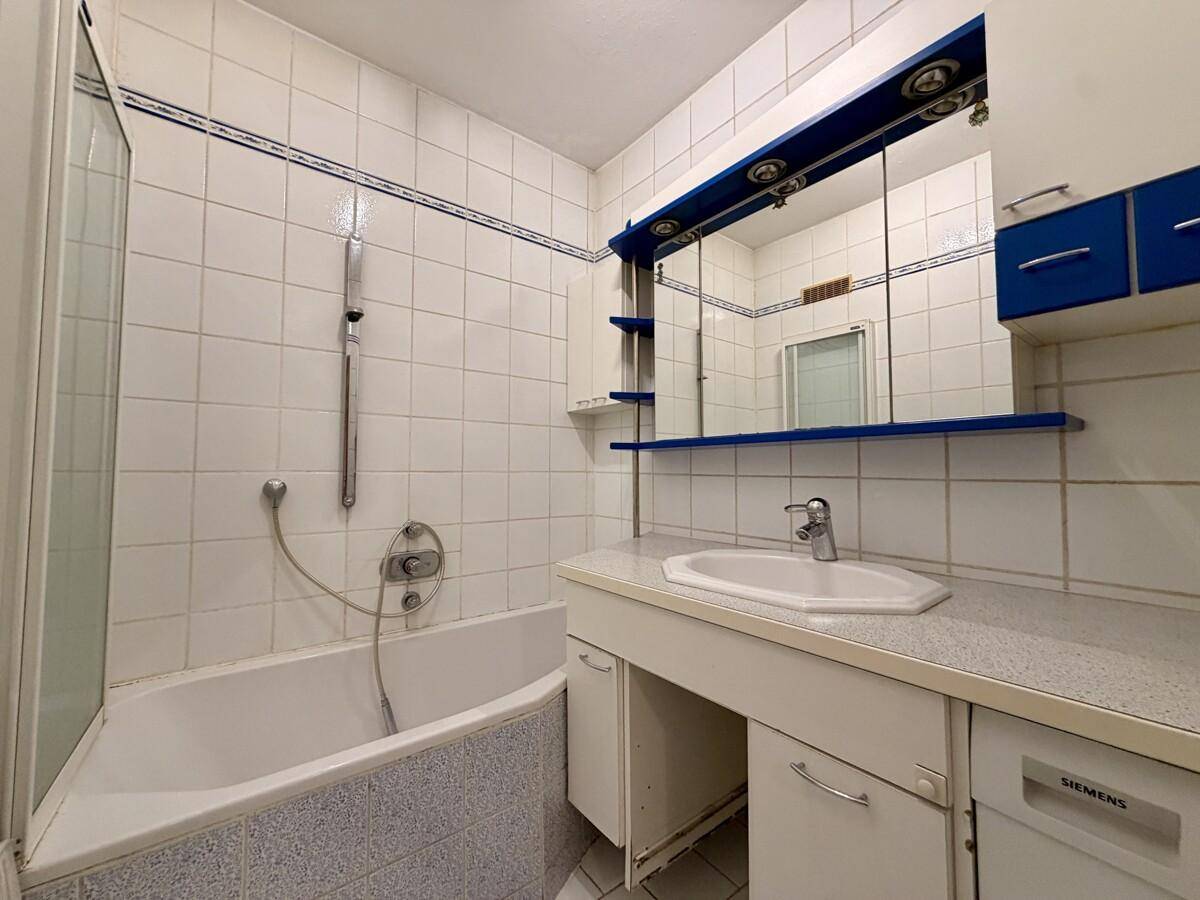 Badezimmer mit Badewanne, Waschbecken und blauen Akzenten, gefliest in Weiß.