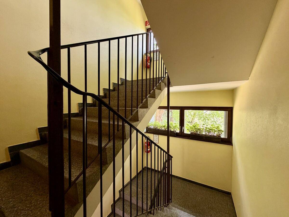 Treppenhaus mit Steinstufen, schwarzem Geländer und gelben Wänden.