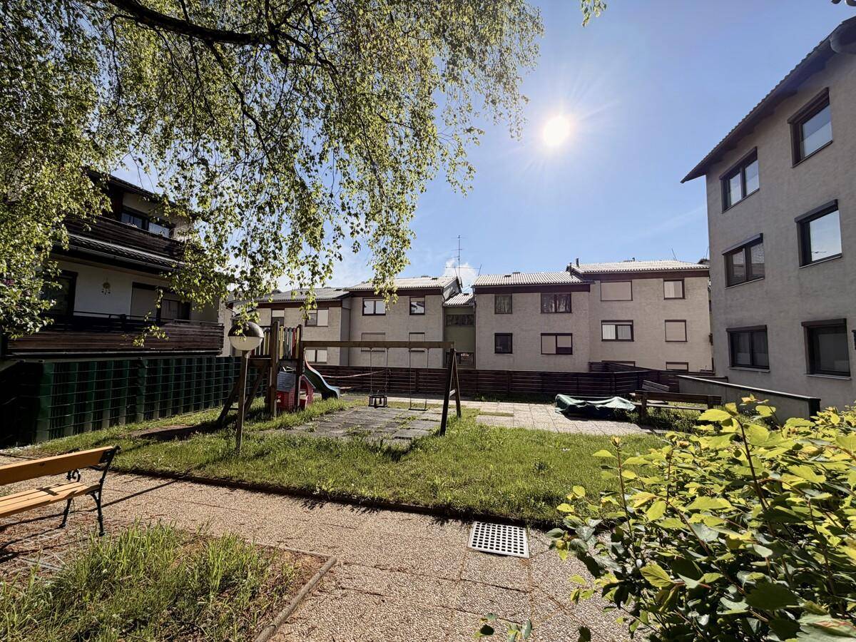 Gemeinschaftsgarten mit Spielplatz, Rasenfläche und Sitzbank zwischen den Wohngebäuden.