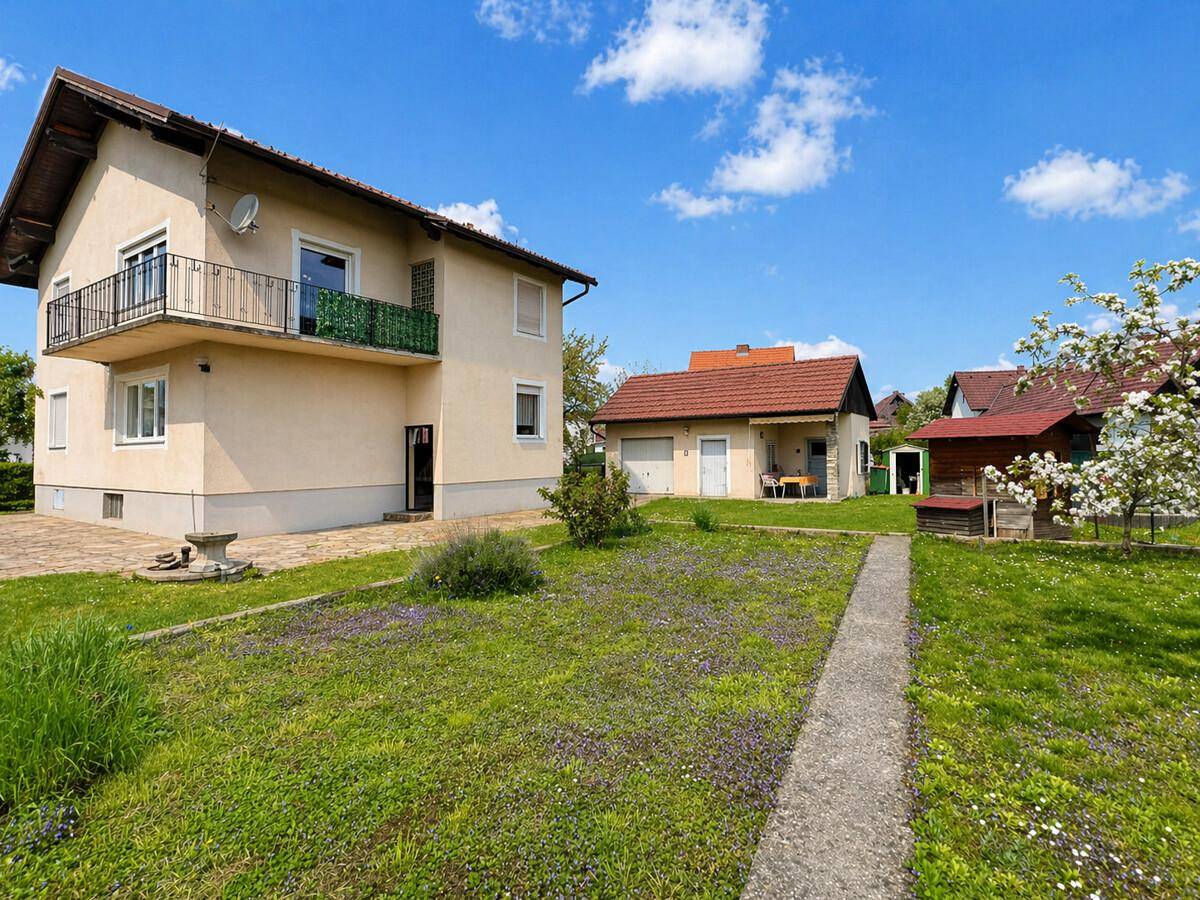 Weitläufiger Gartenbereich mit Rasen, blühendem Baum und Blick auf das Wohnhaus sowie eine separate Garage.