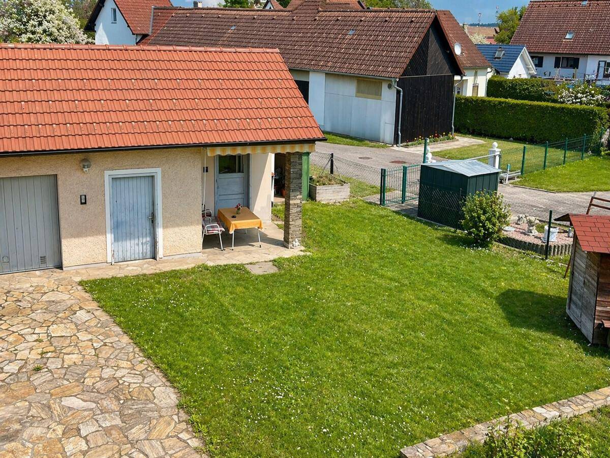 Blick von oben auf den Gartenbereich mit Rasenfläche, Garage und einer kleinen überdachten Terrasse.