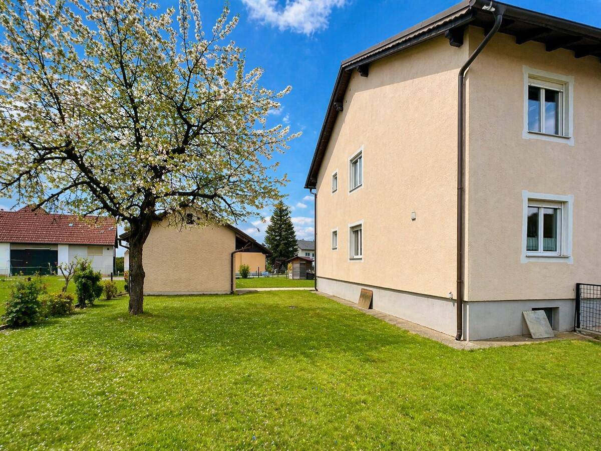 Weitläufige Rasenfläche neben dem Haus mit blühendem Baum und weiteren Gebäuden im Hintergrund.