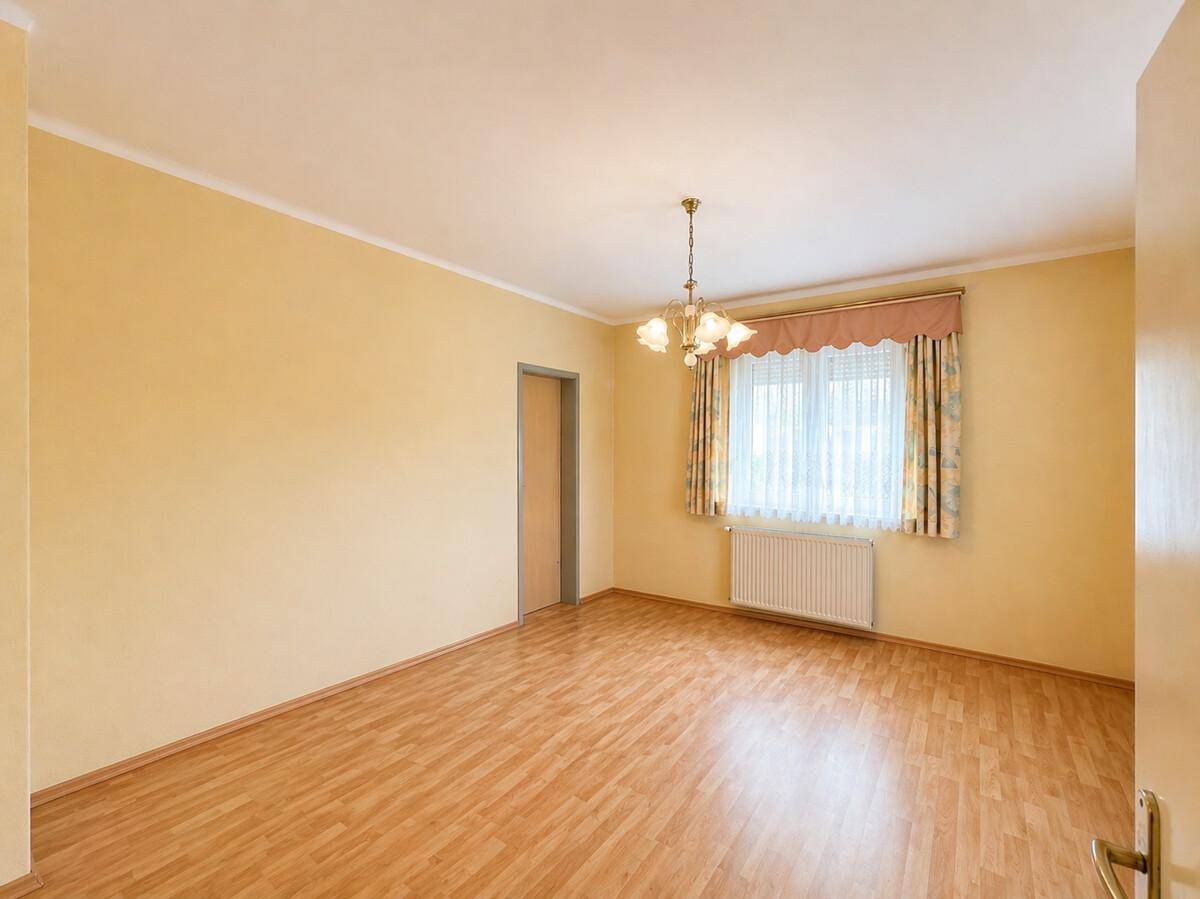 Leeres Schlafzimmer mit hellem Laminatboden, Fenster und Heizkörper, bereit zur individuellen Gestaltung.